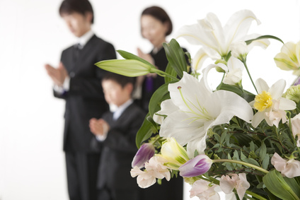 喪服姿で合掌する家族と祭壇の花